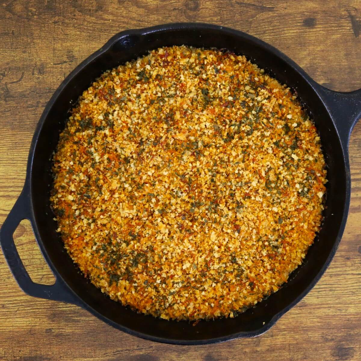 A cast iron pan filled with a crumbly, golden-orange dish sits on a wooden table.