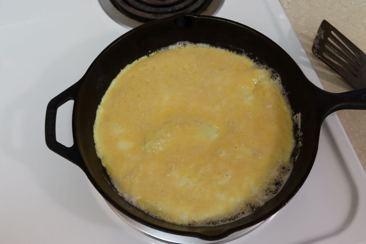 Partially cooked scrambled egg mixture covering the bottom of a cast iron skillet.