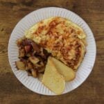 An omelette with smoked paprika and shredded cheese on top sitting on white plate with homefried and semolina toast on the plate next to it.
