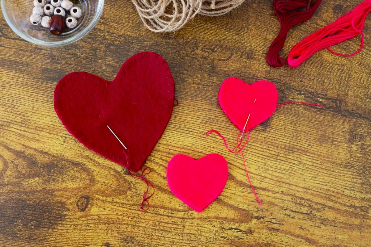 Felt heart cutouts sewn part way around the edges with twine, thread, and beads visible to the side of them.