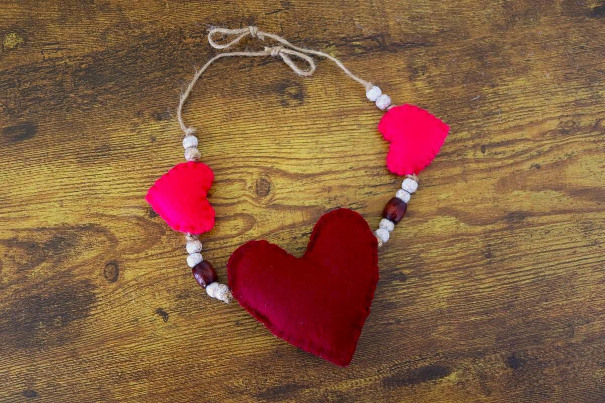 A garland made from one large red heart, two small pink hearts, and beads strung on jute twine.