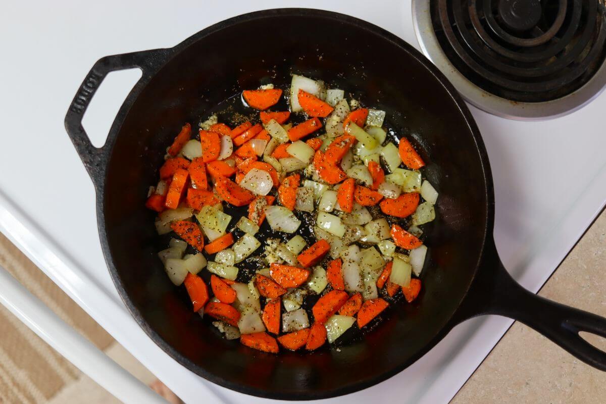 Chopped and seasoned carrots and onions cooking in a cast iron pot.