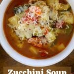 Vegetable soup topped with shredded parmesan cheese in a white bowl. Text overlay reads 'zucchini soup the italian way'.
