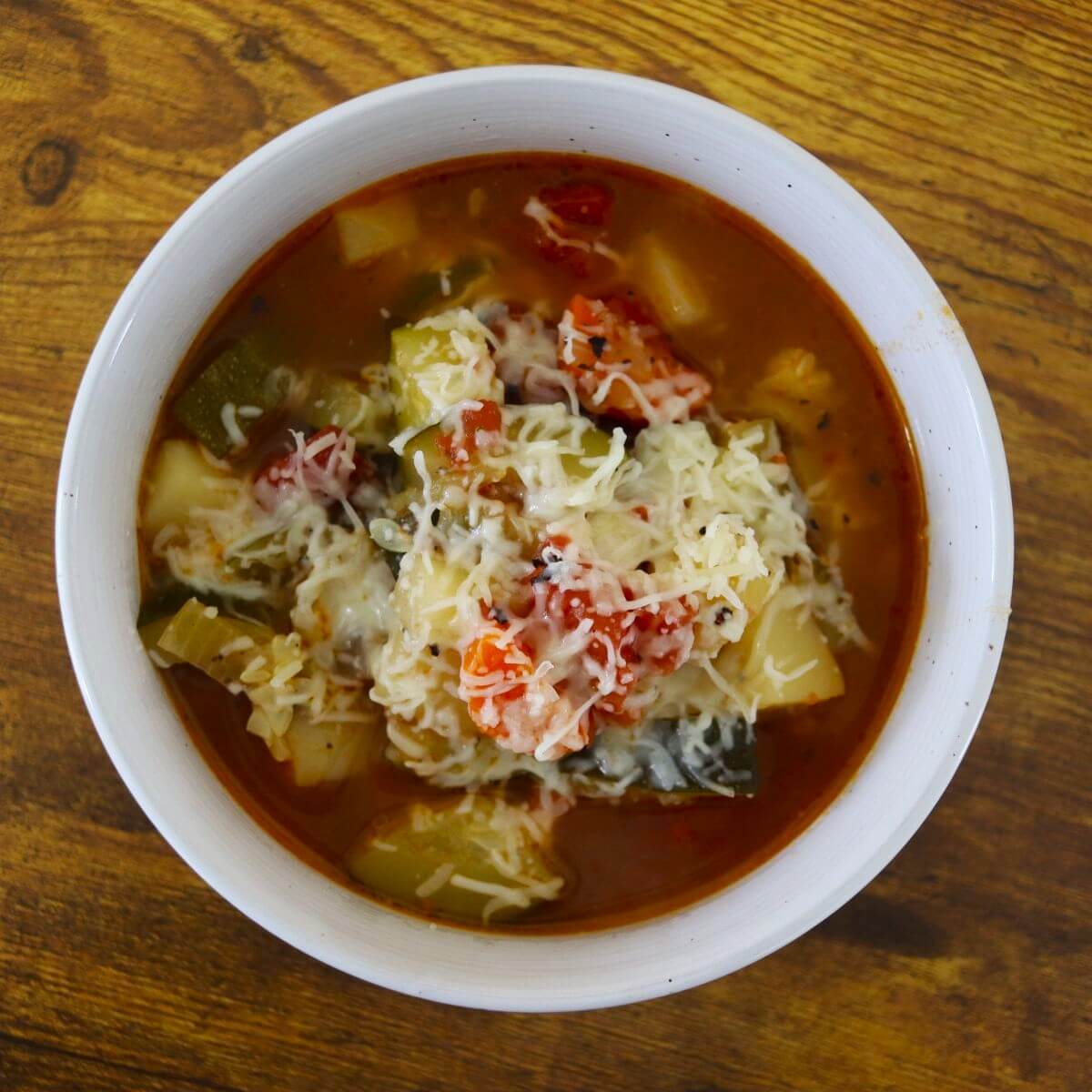 Vegetable soup topped with shredded parmesan cheese in a white bowl.