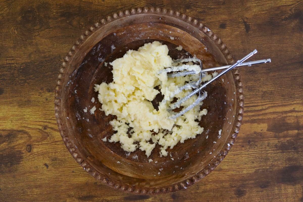 Creamed butter mixture in a wooden bowl with beaters in it.
