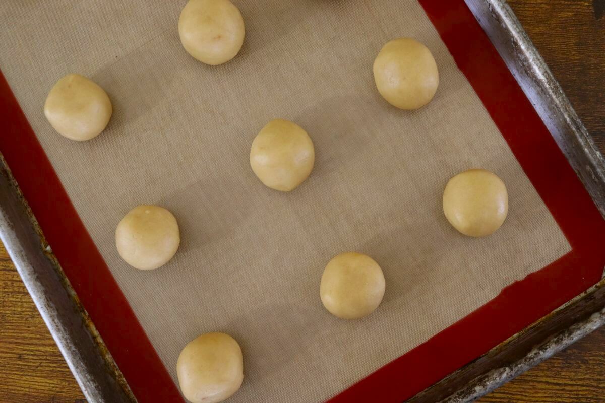 Round balls of dough on a silicone mat lined baking sheet.