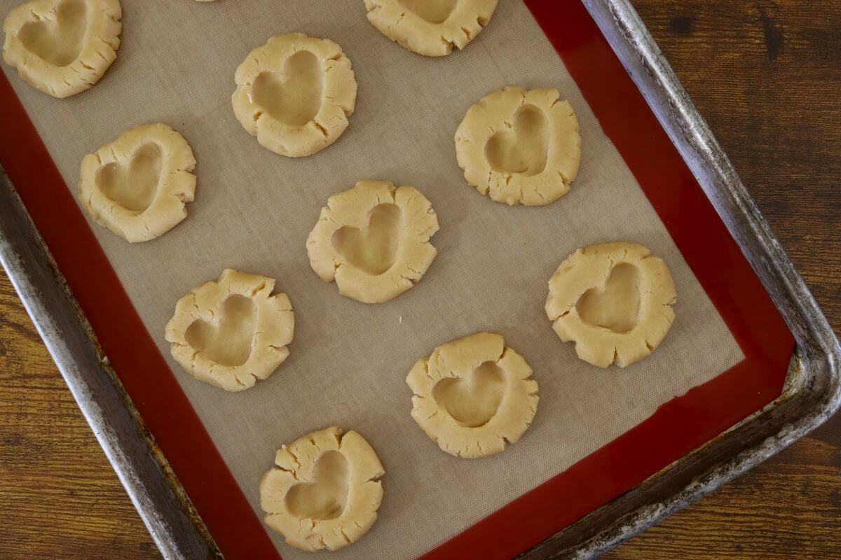 Flat, round pieces of dough with heart shapes pressed in the top on a silicone lined baking sheet.