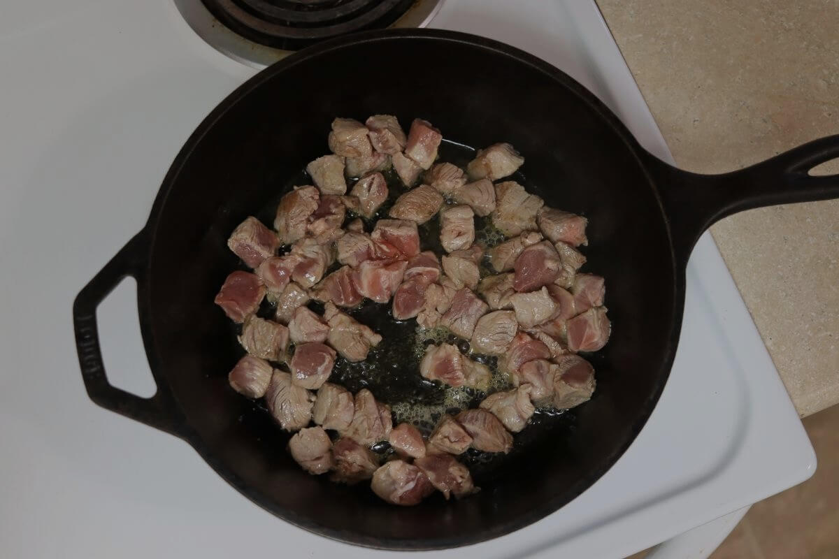 Partially browned pork cubes in a cast iron pot.