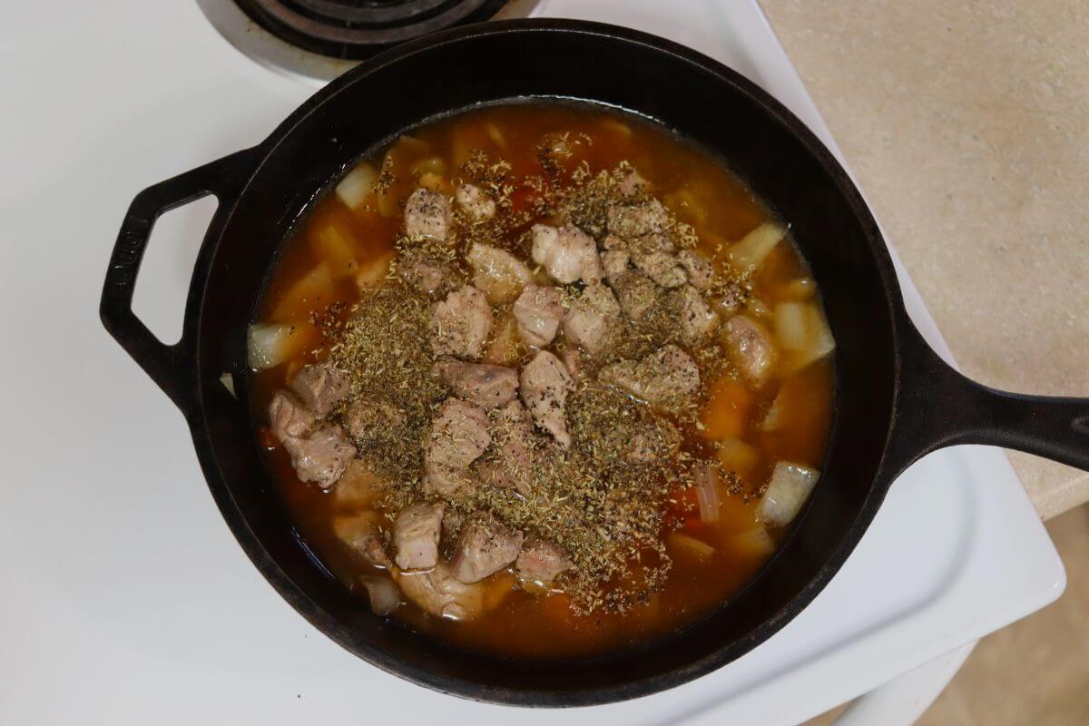Cubed vegetables and pork in a cast iron pot of broth with seasoning on top.