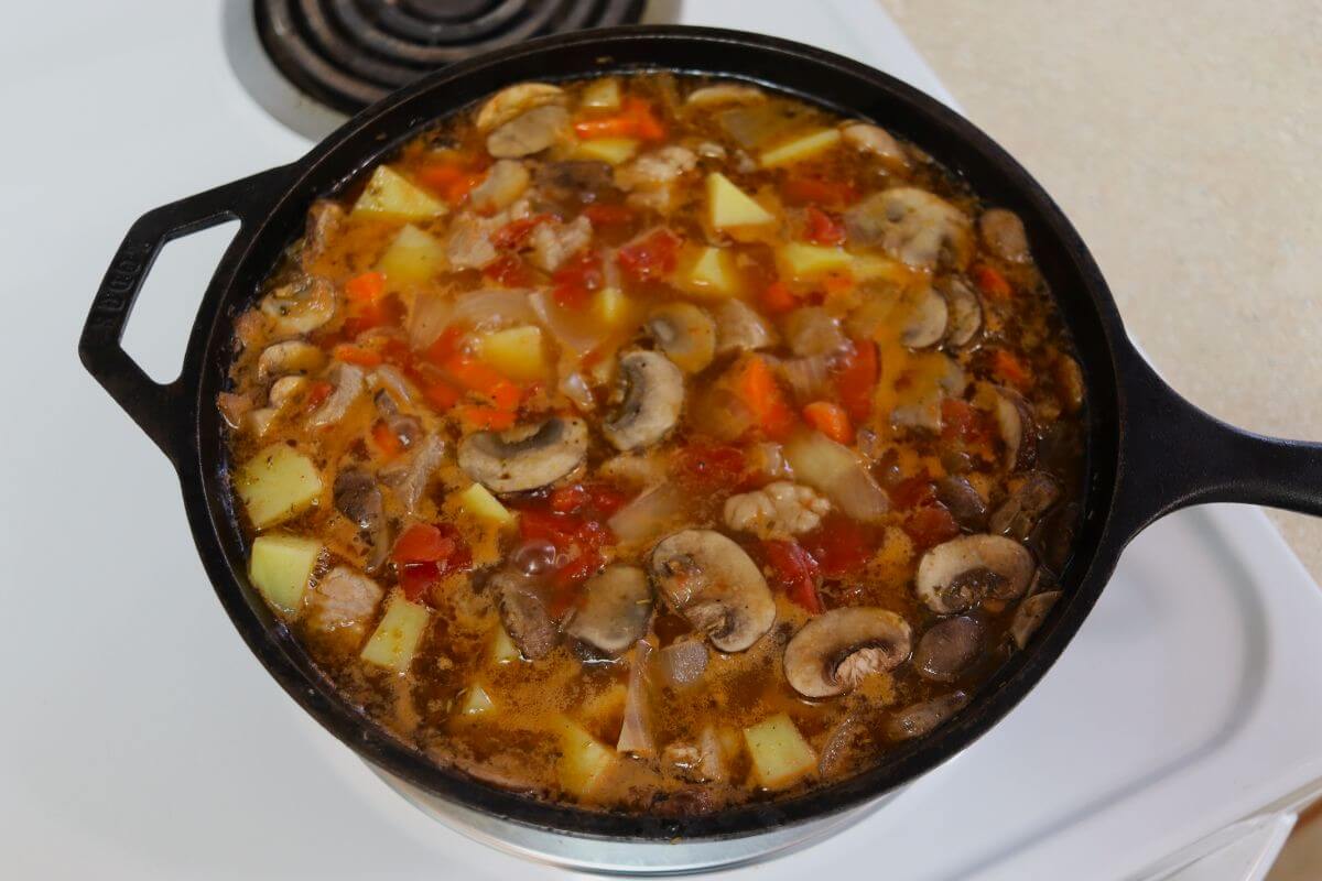 Chopped vegetables and pork in a cast iron pot of broth.