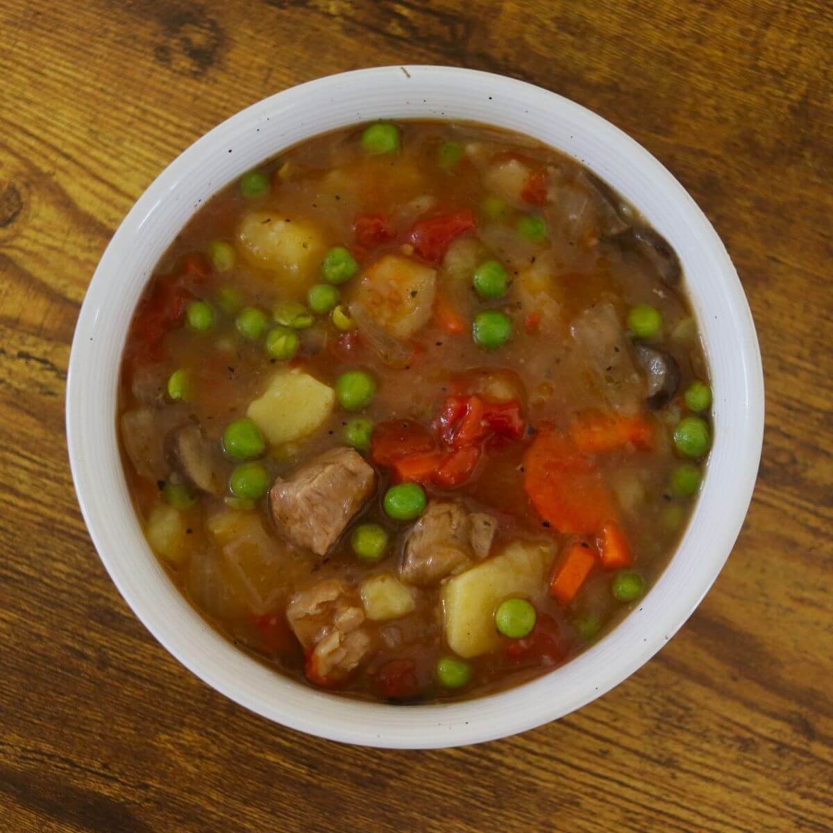 A bowl of pork stew sitting on a wooden surface.