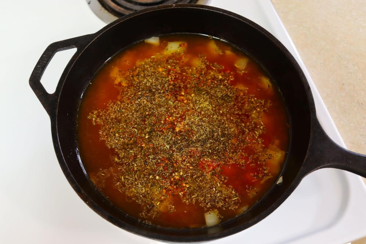 Red broth with vegetables visible in it and topped with seasoning in a cast iron skillet.