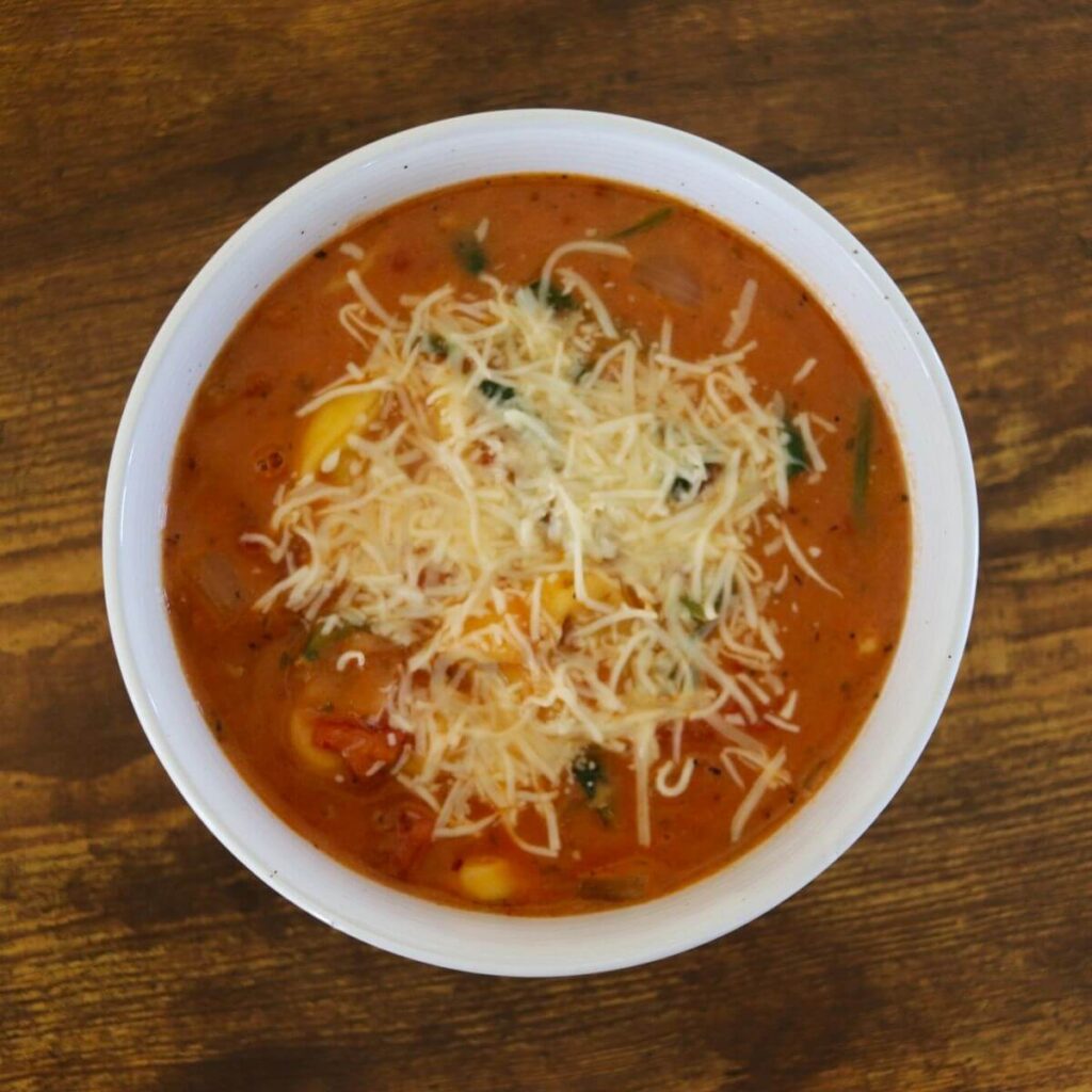 Tomato based soup topped with shredded cheese in a white bowl.