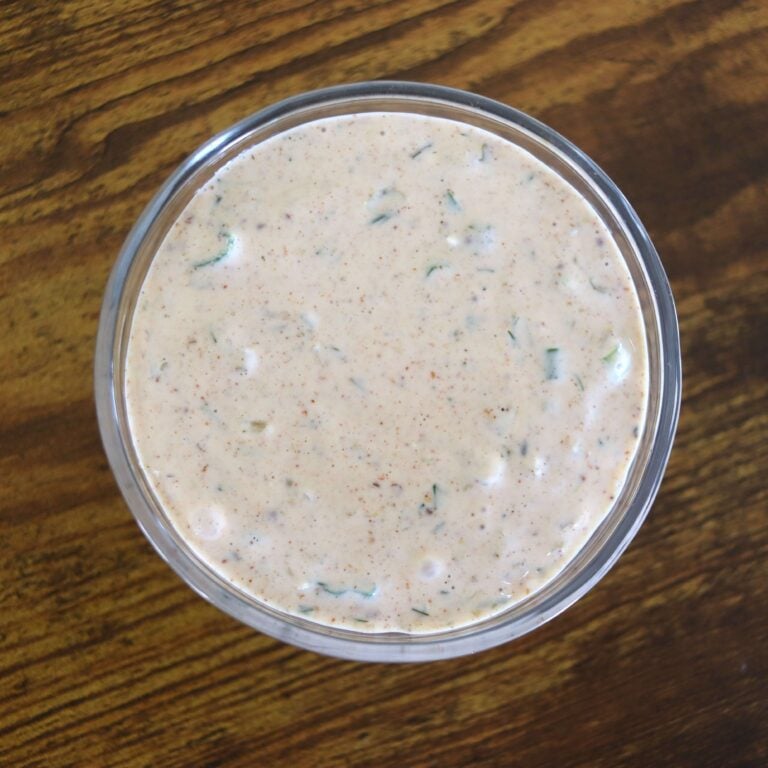 A glass dish with a creamy sauce with herbs visible in it on a wooden surface.