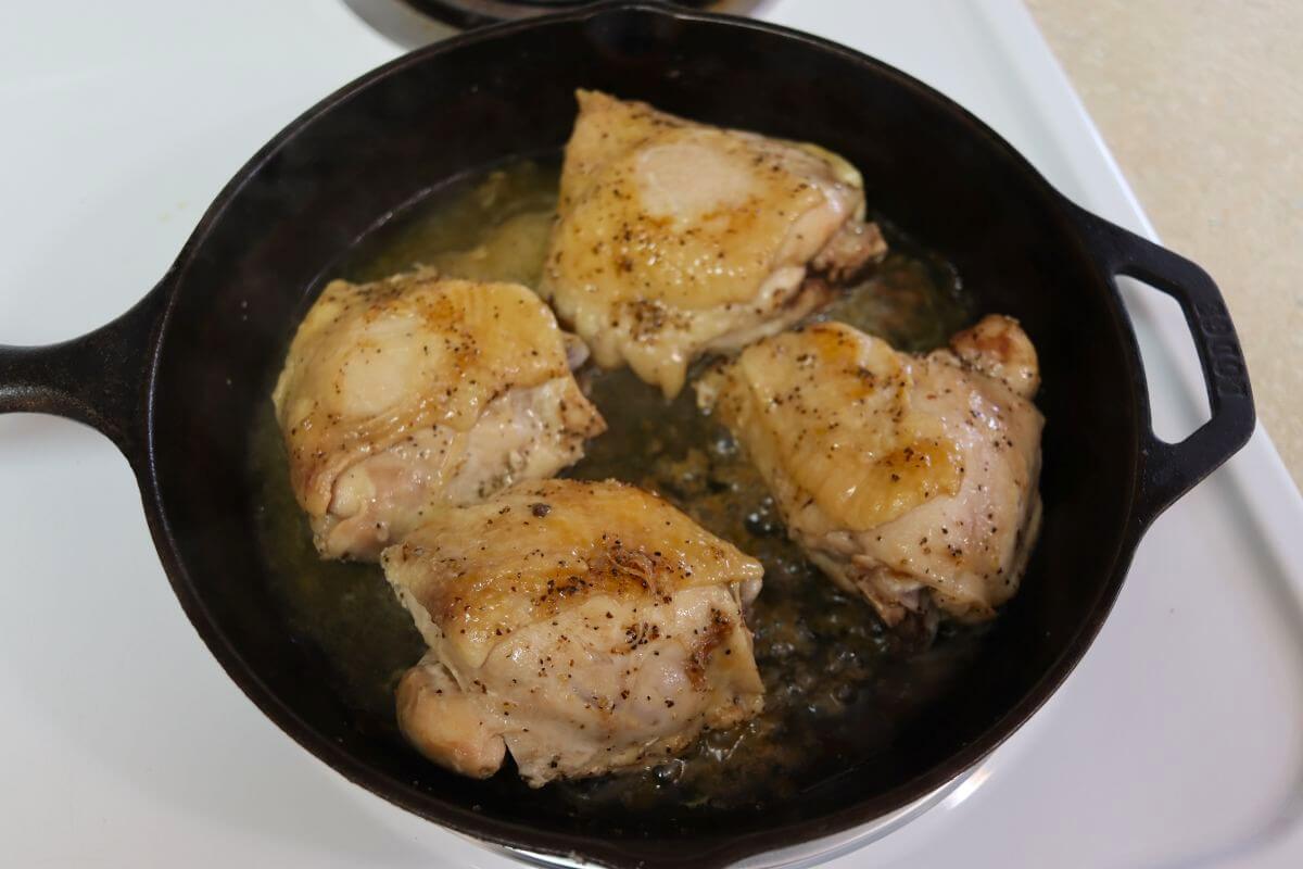 Four chicken thighs simmering in a cast iron skillet.