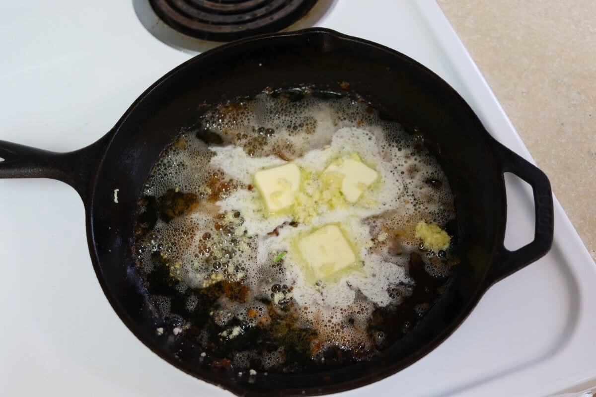 Chicken drippings, butter, and pressed garlic in a cast iron skillet on a stovetop.