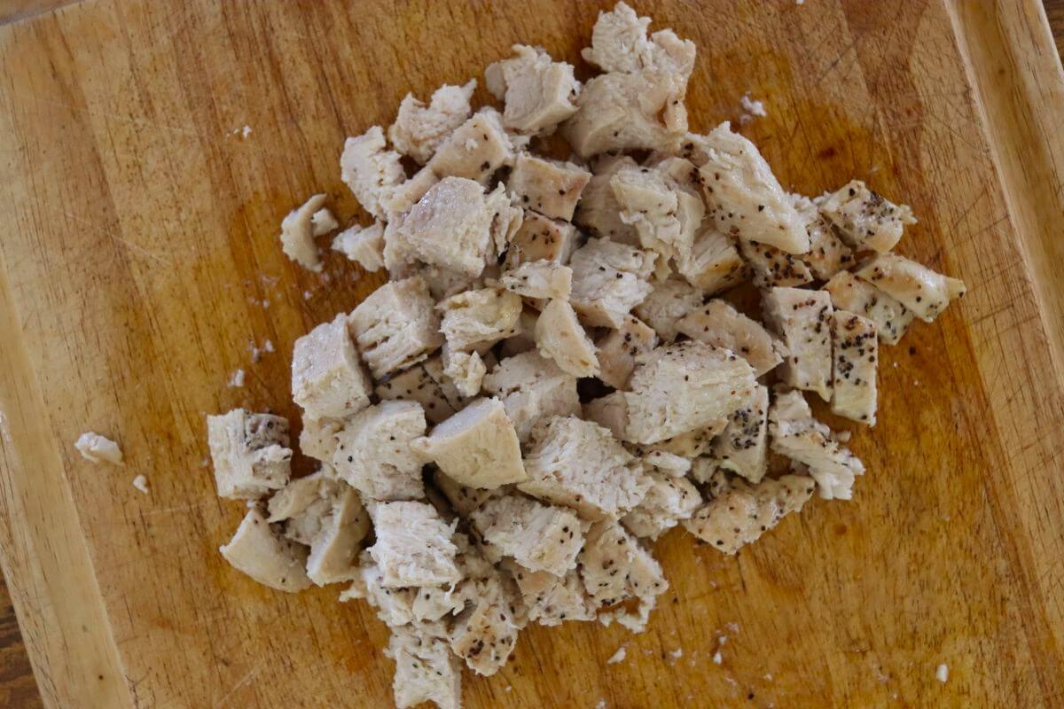 Chopped cooked chicken breast cut into bite-size pieces on a wooden cutting board.