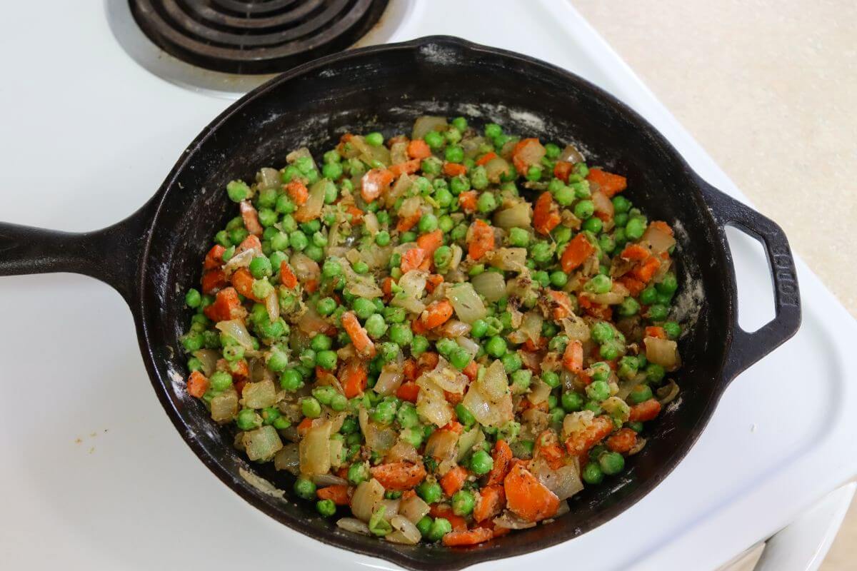 Flour stirred into carrots, onions, and peas in a cast iron skillet to form the base of the sauce.