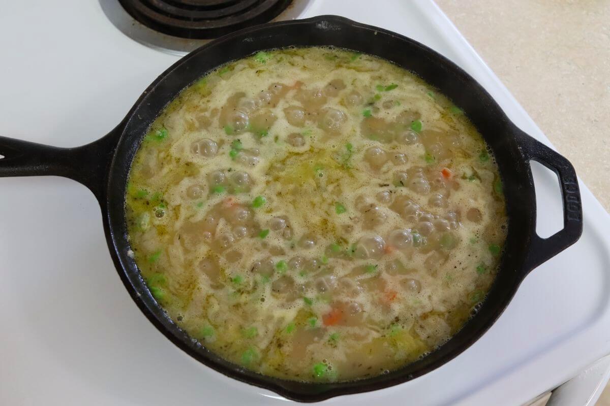 Chicken broth added to the skillet, simmering with vegetables as the sauce begins to thicken.