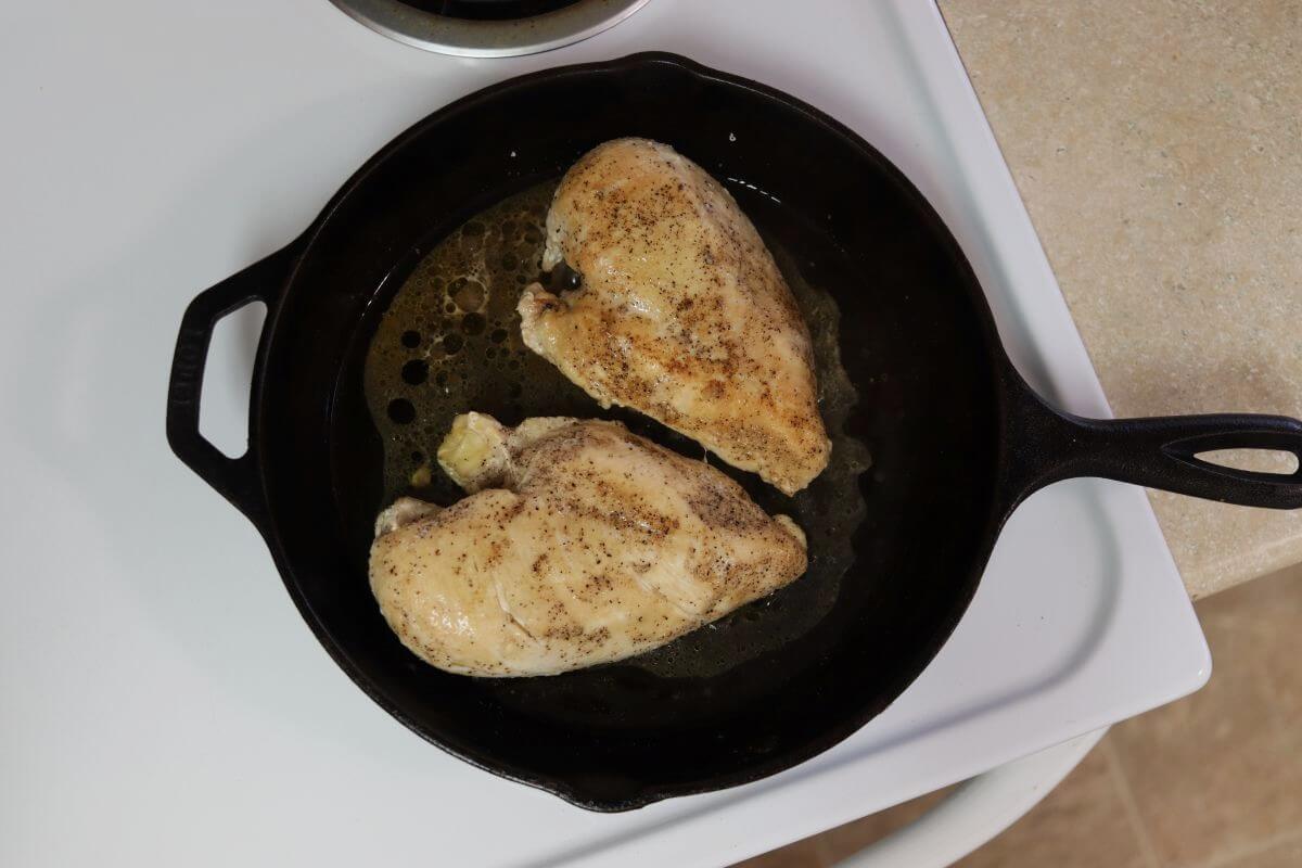 Two seasoned chicken breast cooking in a cast iron skillet.