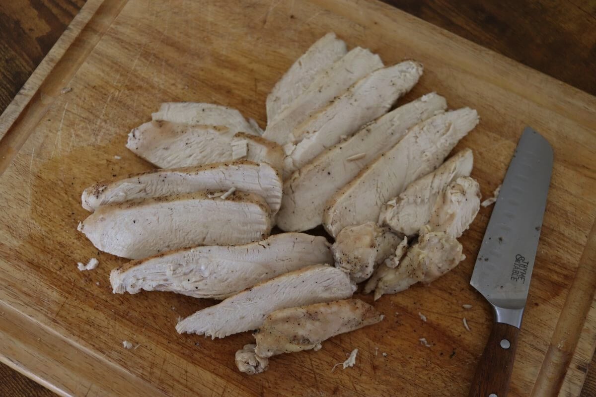 Two rows of sliced cooked chicken breast on a cutting board.