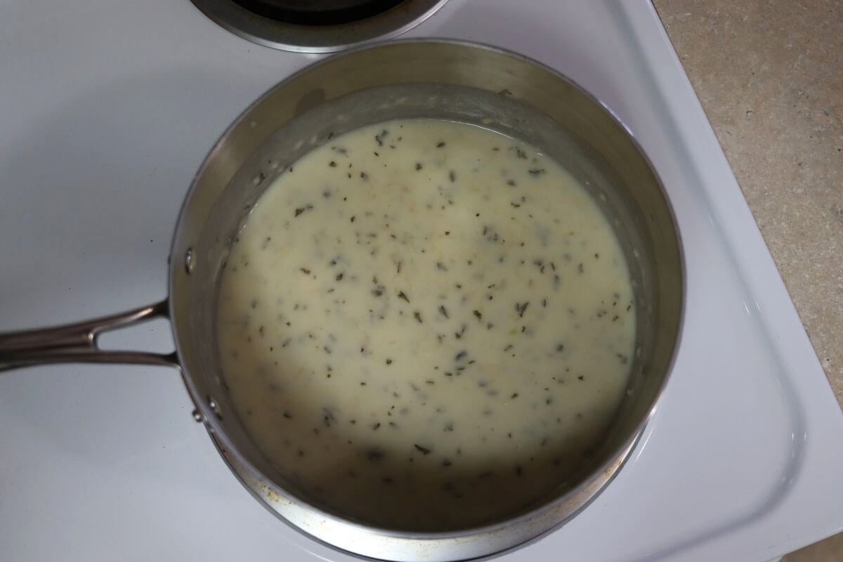 A white sauce with seasoning in it in a saucepan.