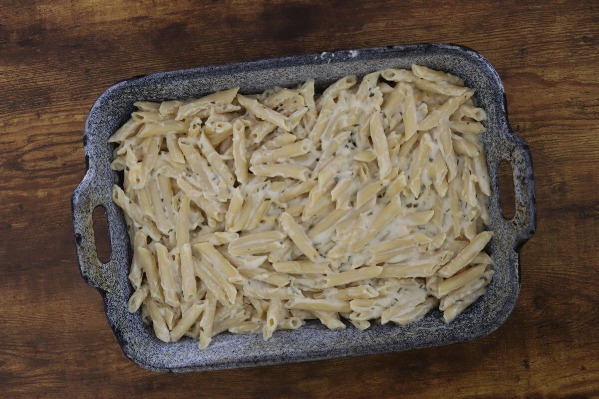 Penne pasta covered in a cheesy white sauce in a baking pan.