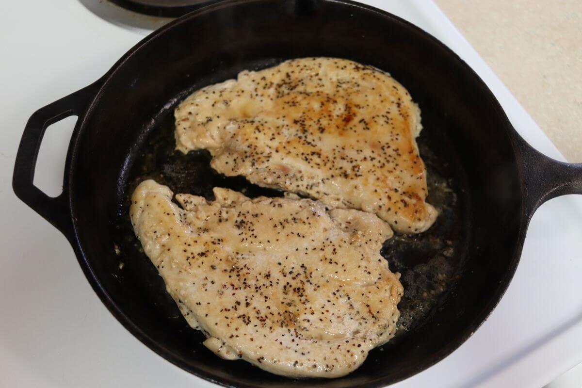Seasoned chicken breasts cooking in a cast iron skillet on the stove.