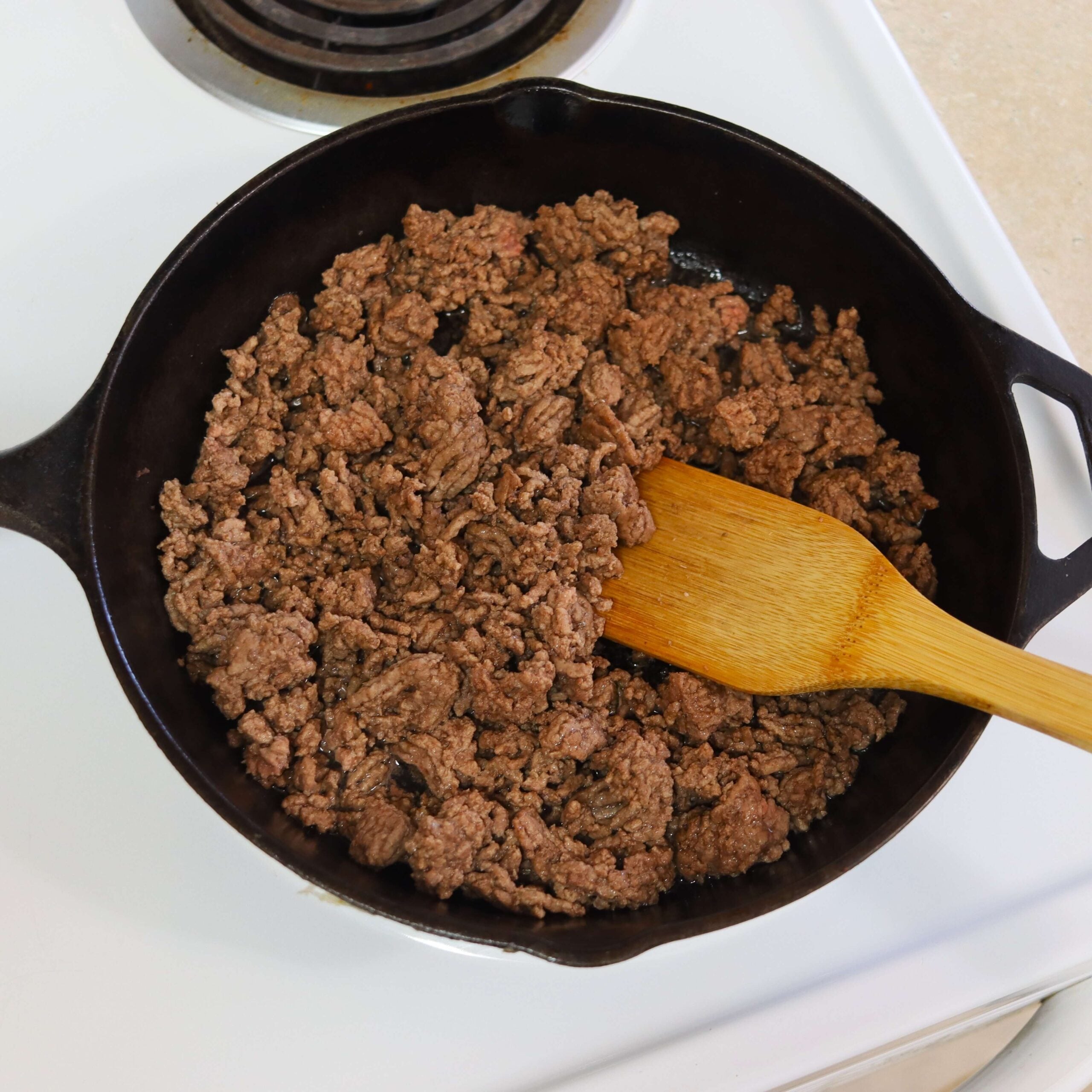Ground beef browning evenly in a cast iron skillet on the stovetop.