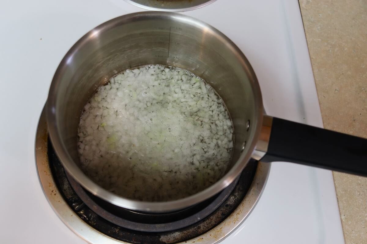 Finely chopped onions simmering in white wine in a small saucepan.