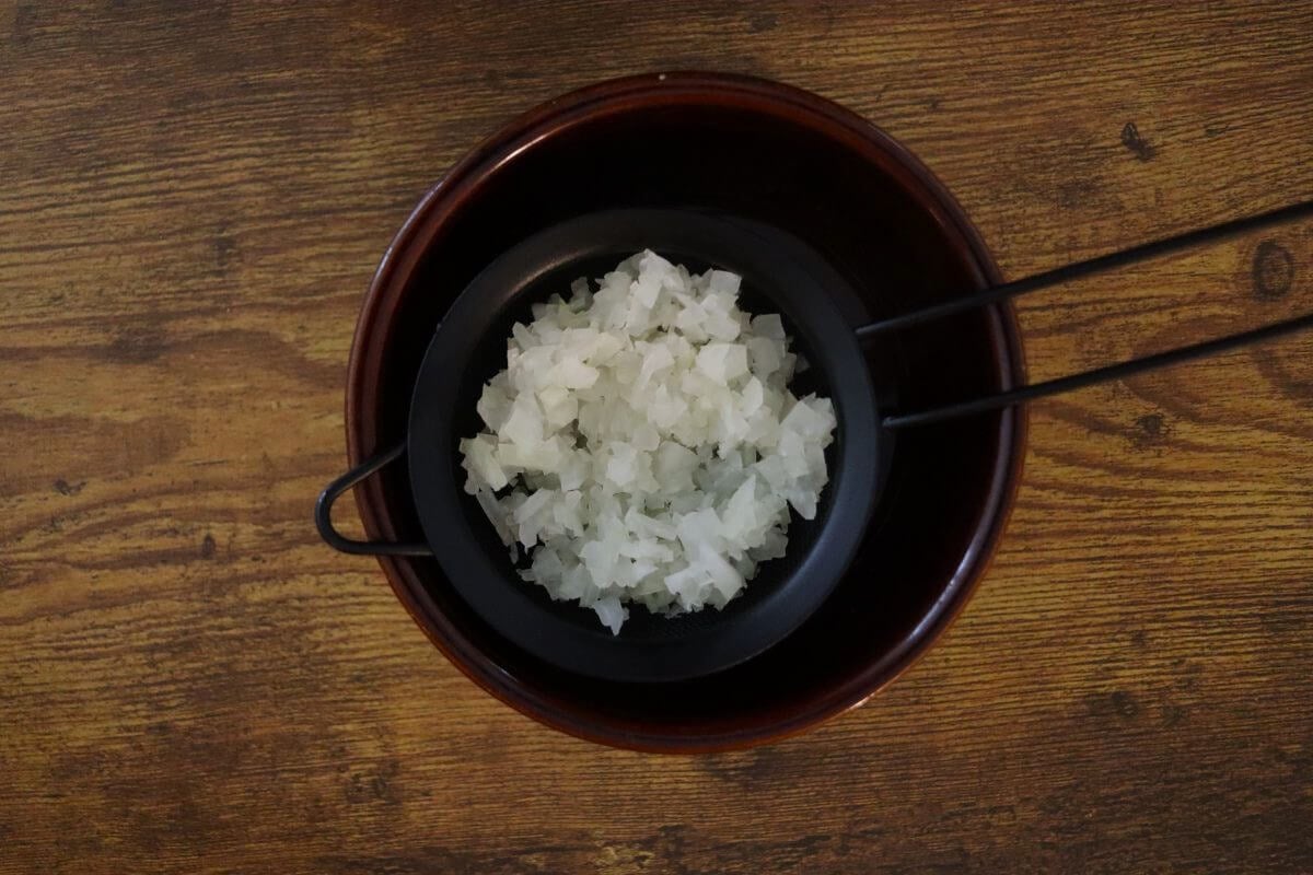 Finely chopped onions in a sieve sitting over a bowl.
