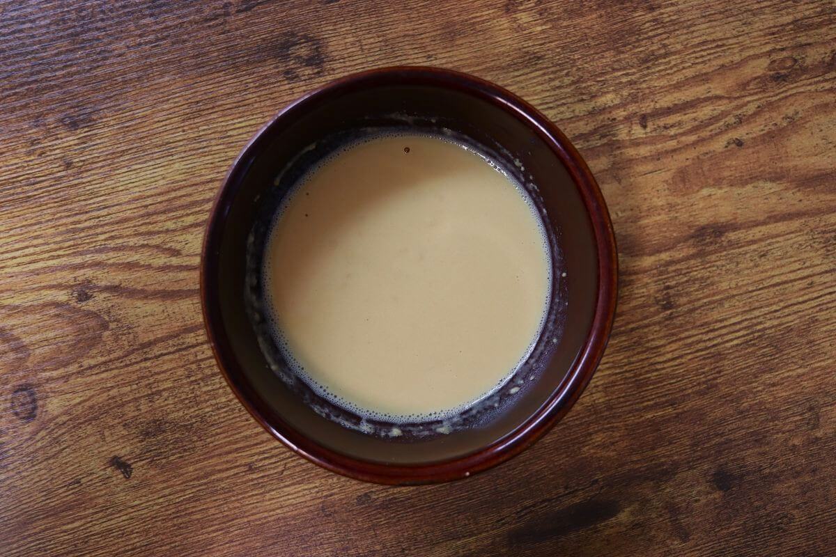 Small bowl of mustard colored liquid sitting on a table.
