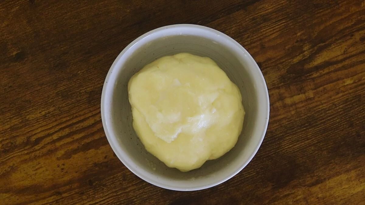 A hand-shaped ball of butter in a white bowl on a wooden table.