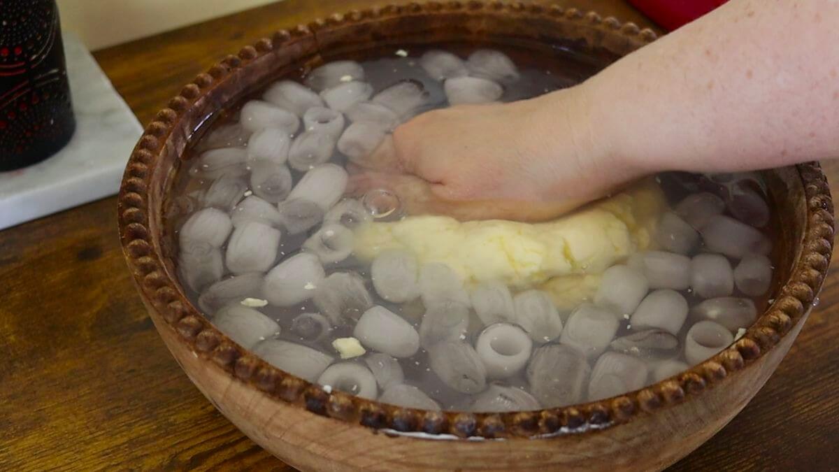 A hand squeezing a clump of butter in a bowl of ice water.
