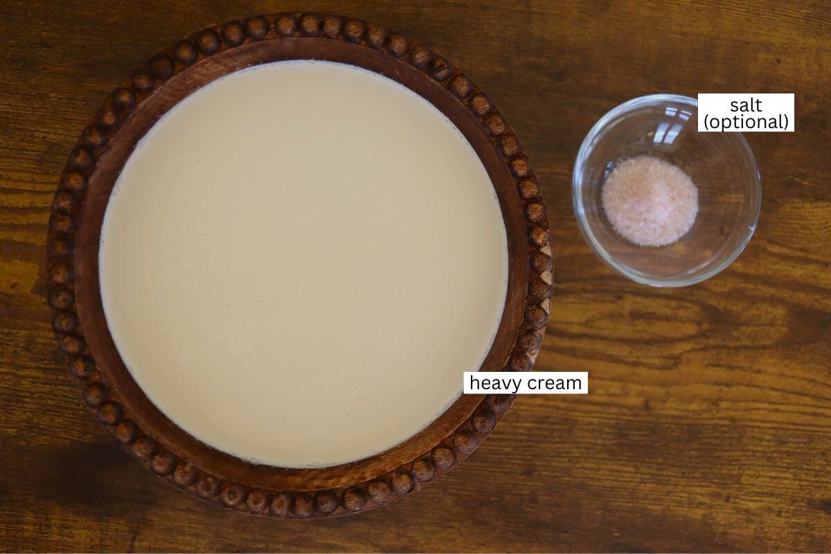 A wooden bowl filled with heavy cream sits on a wooden surface next to a small glass bowl containing pink salt, labeled as optional.