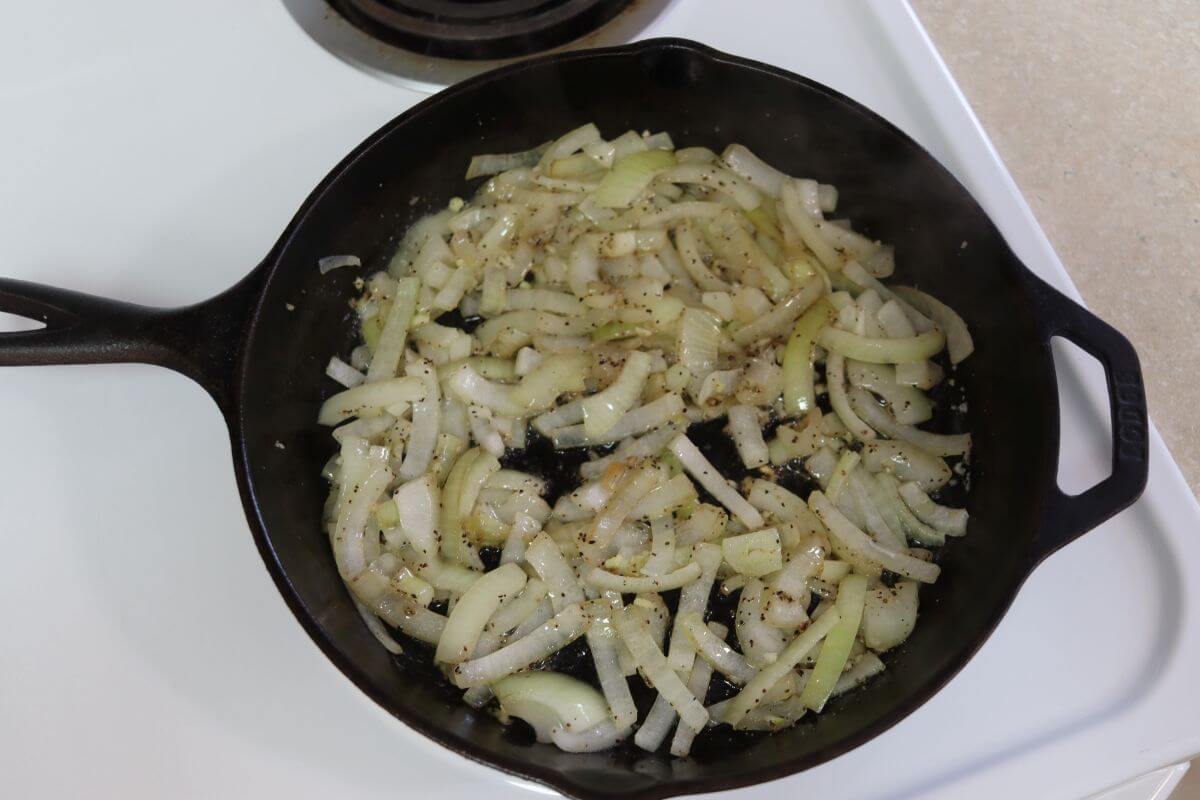 Sliced onions cooking in butter with pepper in a cast iron skillet on the stovetop.