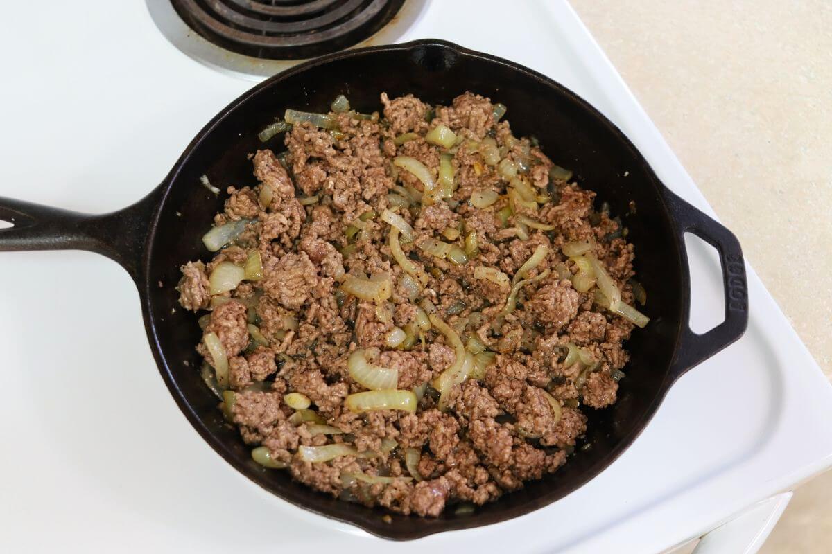 Ground beef cooked with onions in a cast iron skillet on the stovetop.