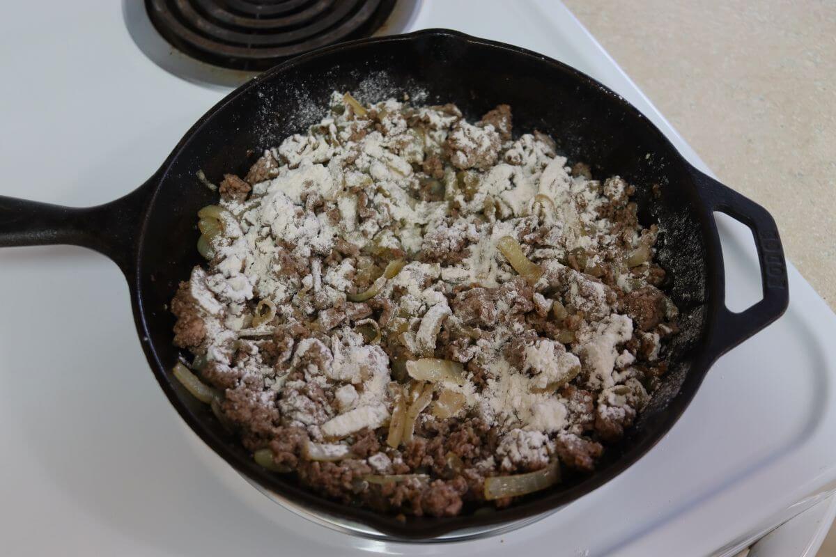 Flour sifted over ground beef and onions in a cast iron skillet.