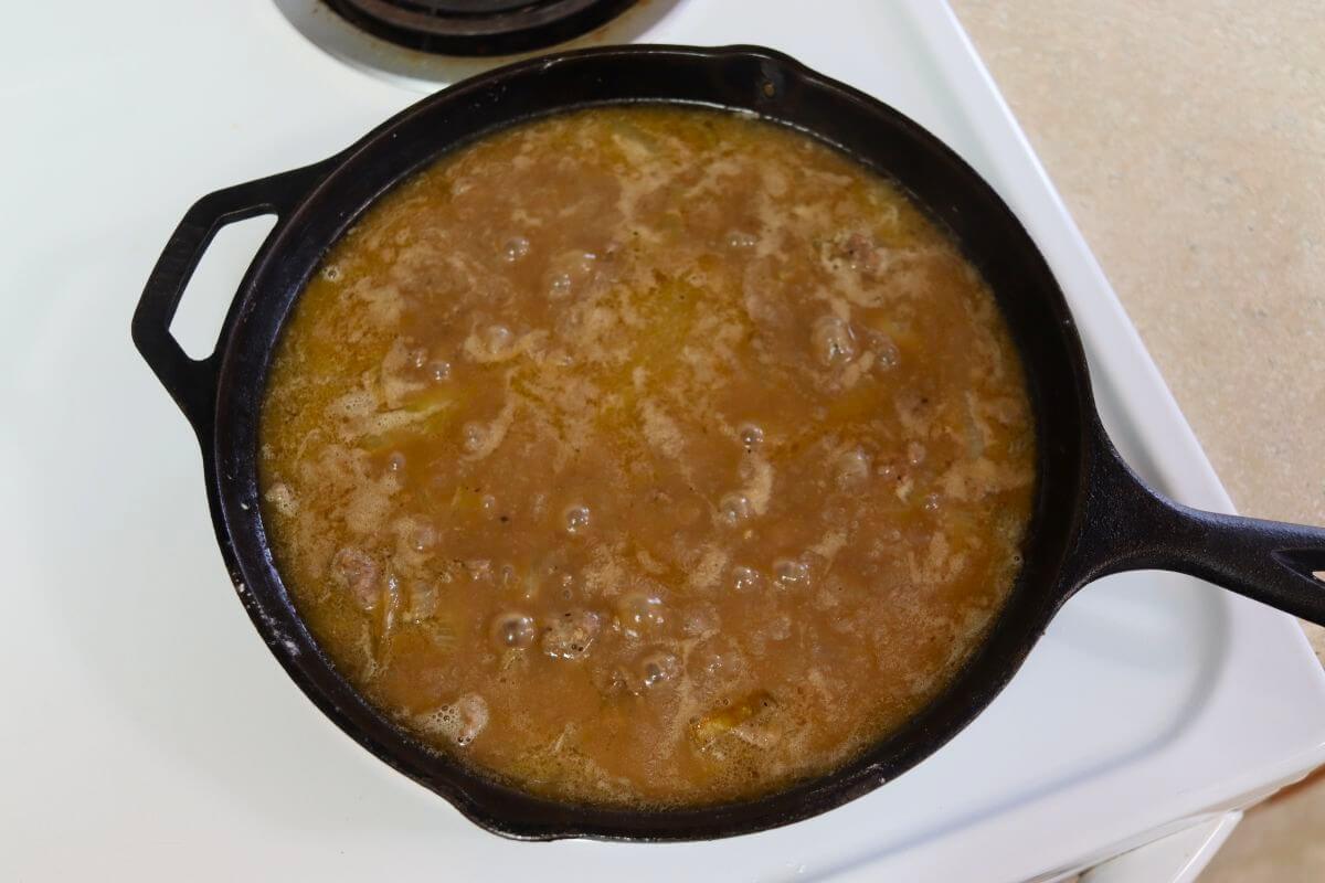 Ground beef gravy simmering in a cast iron skillet on the stovetop.