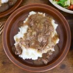 Ground beef and gravy served over mashed potatoes on a brown plate.