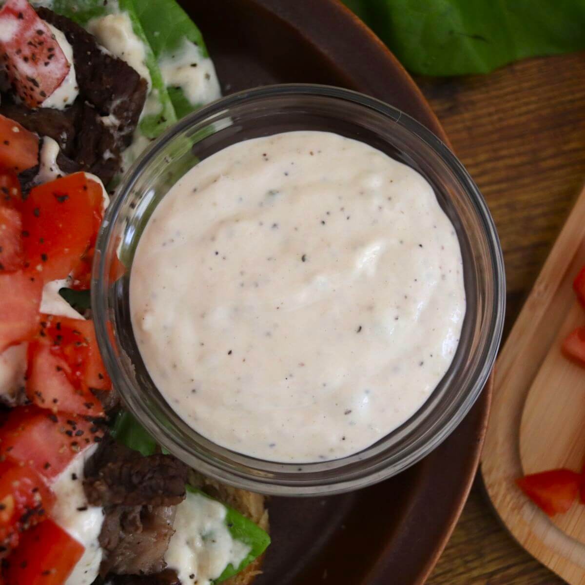 White sauce in a small dish with chopped tomatoes, lettuce, and chopped beef visible next to it.