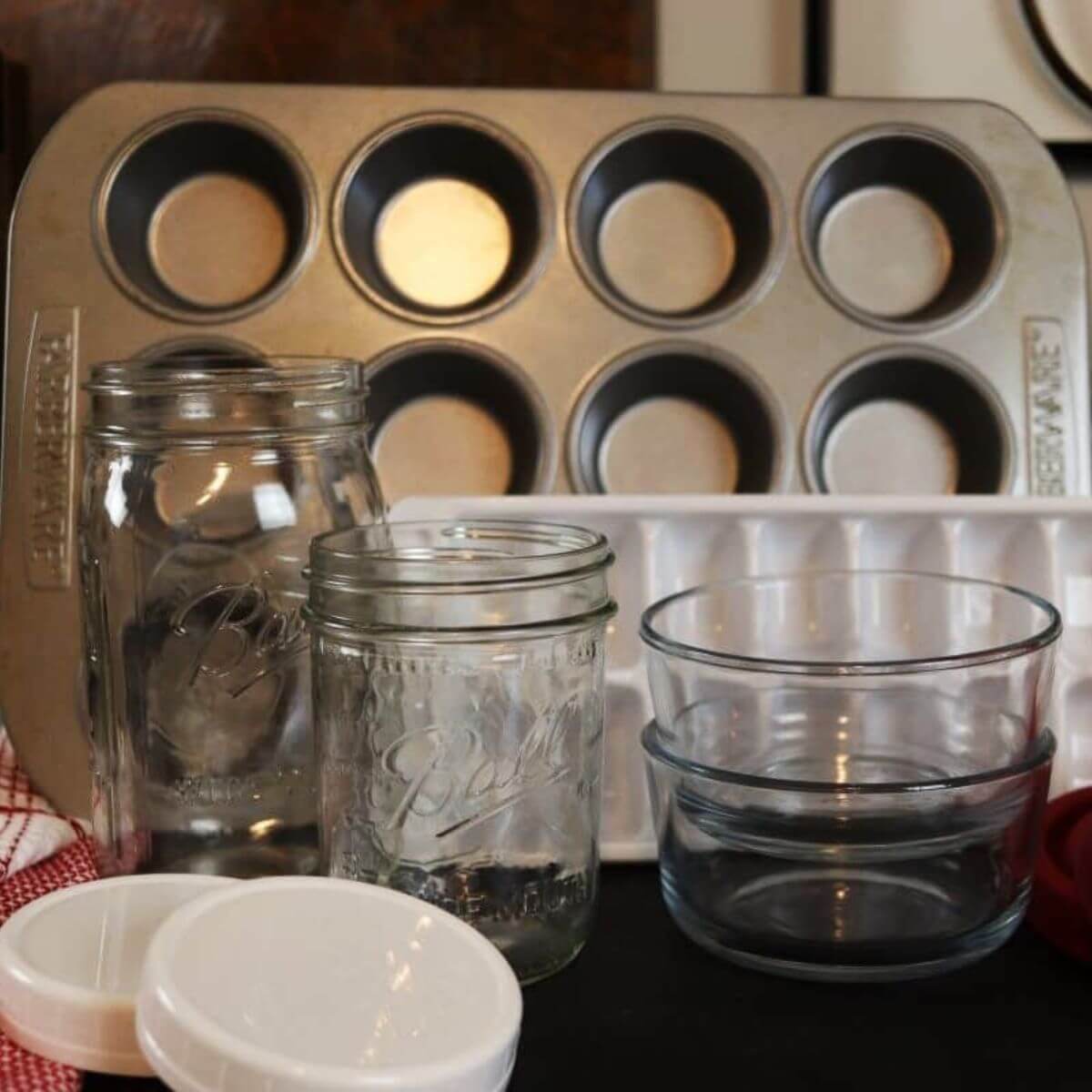 A muffin tin, mason jars and lids, and glass bowls and lids sitting together on a countertop.