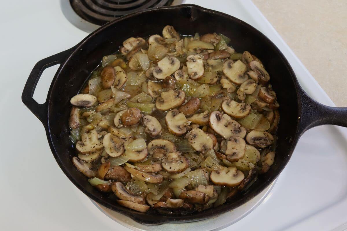 Sliced mushrooms and cooked onions simmering together in a cast iron skillet with visible juices.
