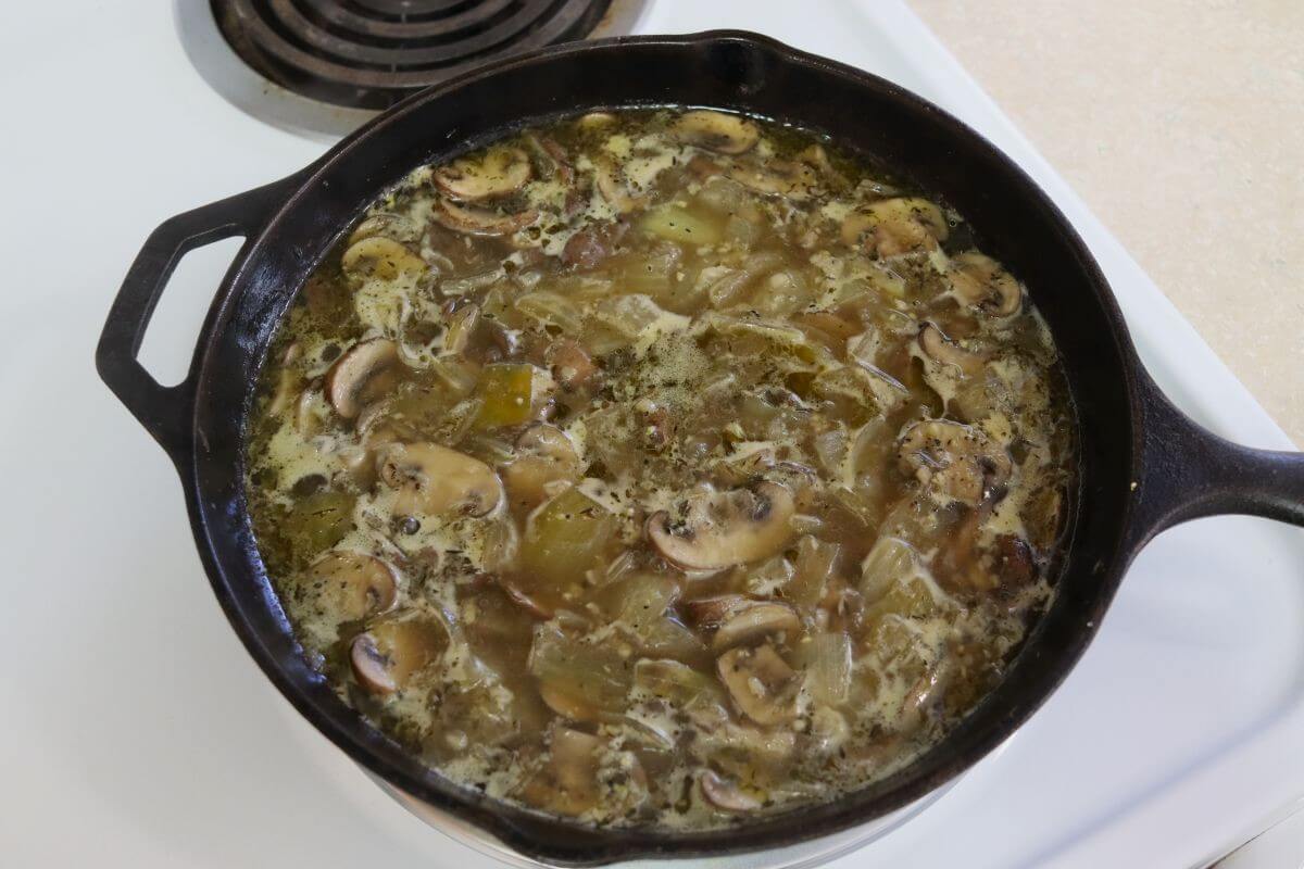 Mushroom and onion mixture simmering in chicken broth and cream in a cast iron skillet on the stove.