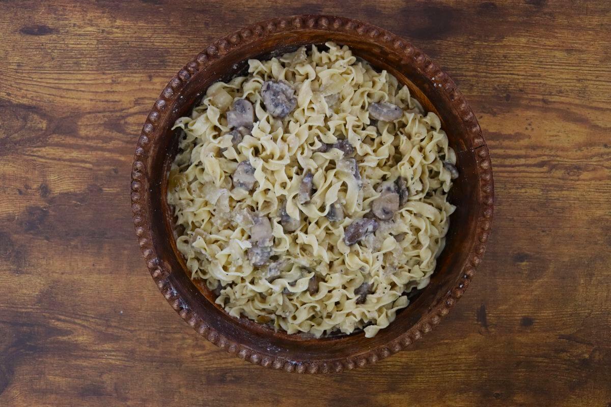 Creamy mushroom pasta made with egg noodles and a cream-based sauce, presented in a brown serving bowl against a wood background.