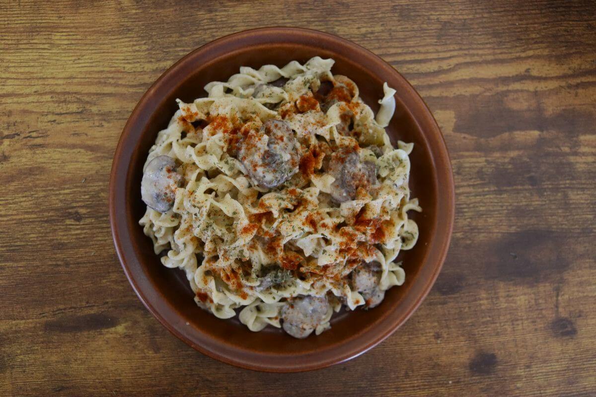 Creamy mushroom pasta with egg noodles, visible mushroom pieces, and a light smoked paprika garnish served on a brown plate on a wooden table.