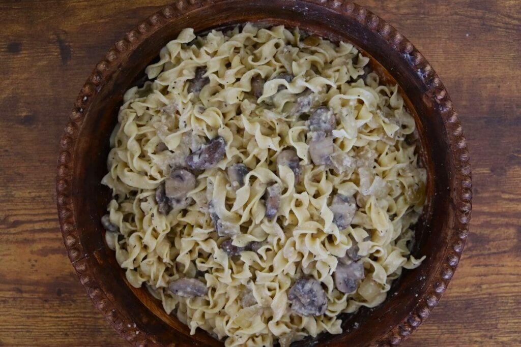 Creamy egg noodles and sliced mushrooms in a wooden serving bowl.