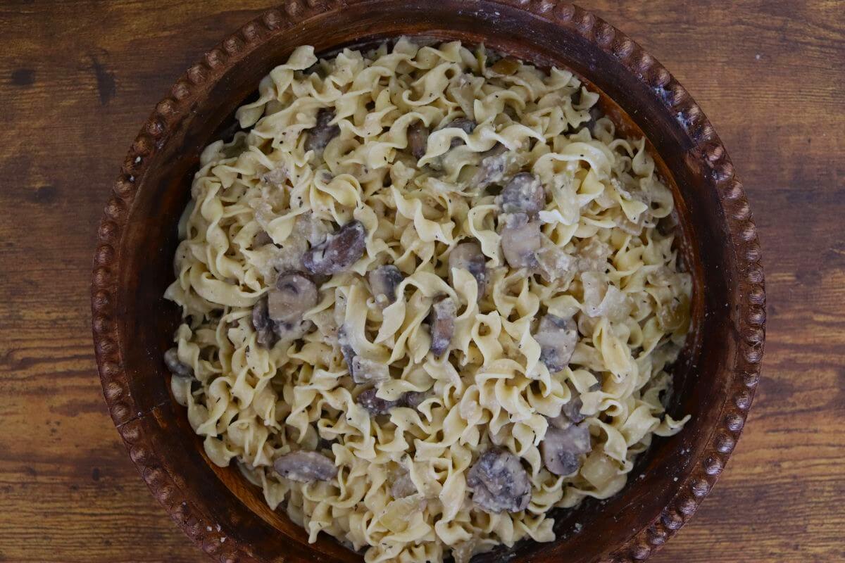 Mushroom pasta tossed with a creamy sauce and egg noodles, served in a rustic brown bowl on a wooden surface.