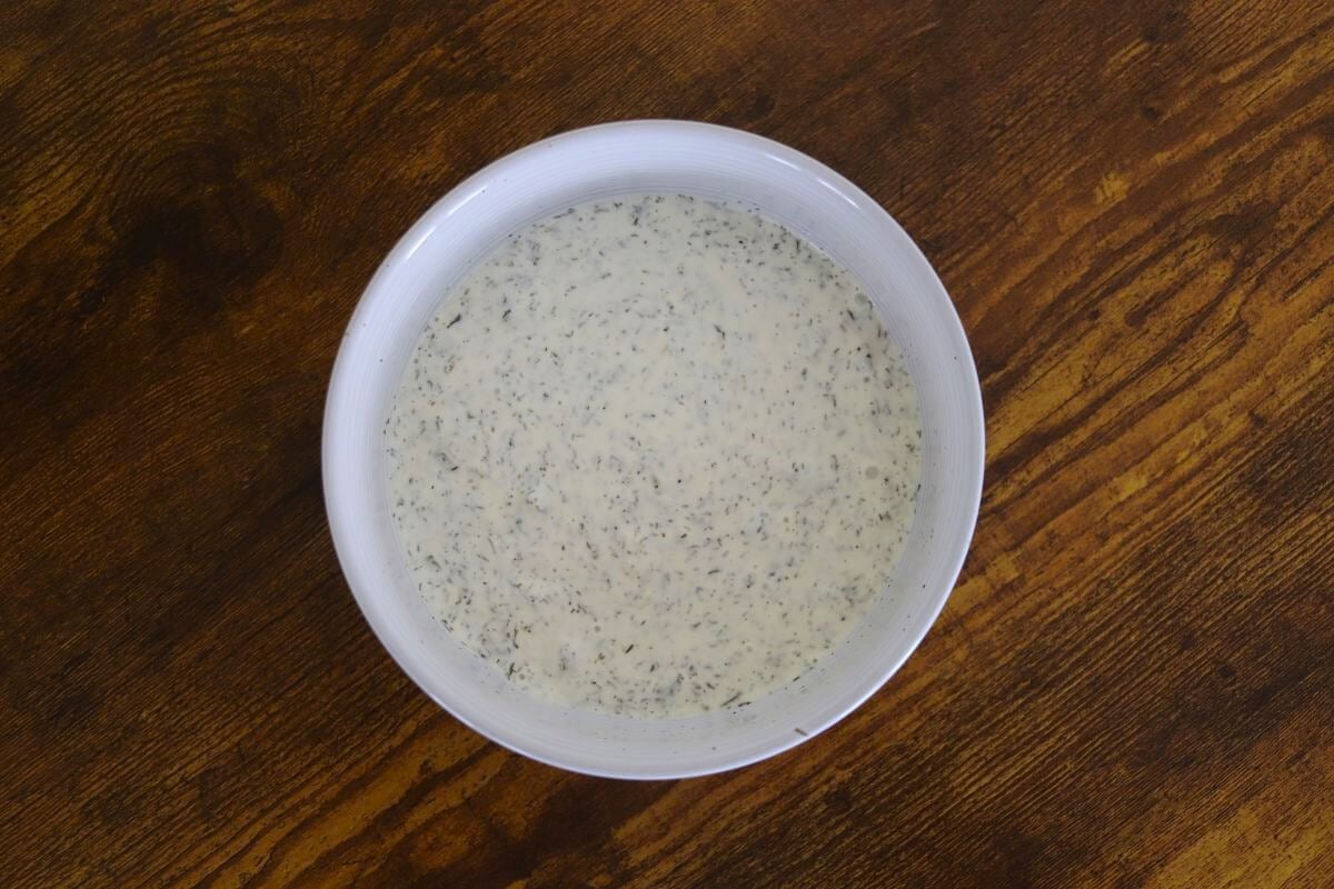 Creamy white sauce with herbs visible in it in a white bowl.
