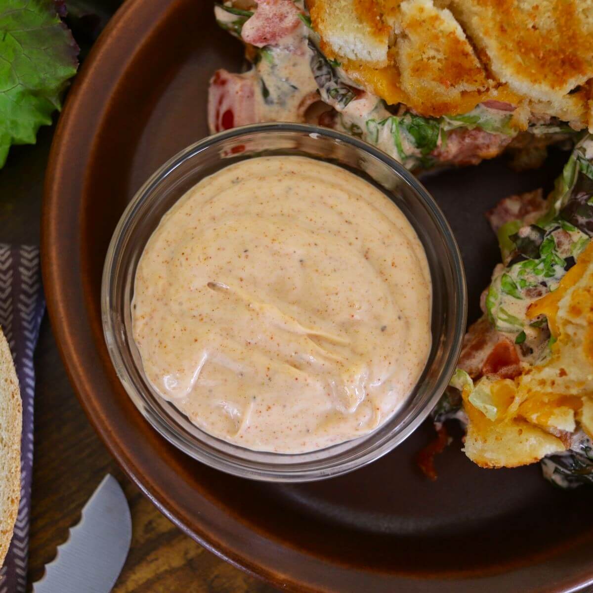 Light orange sauce in a small dish on a plate with a grilled sandwich visible to the side of it.